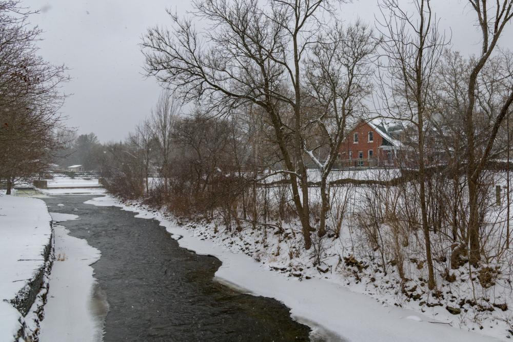 winter scene, river with snow and bare trees with a red barn in background